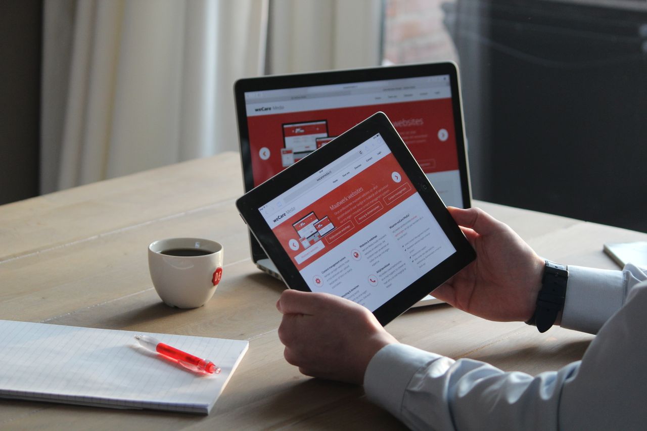 services-01 Business professional using a tablet and laptop with a hot drink, focusing on digital content review.